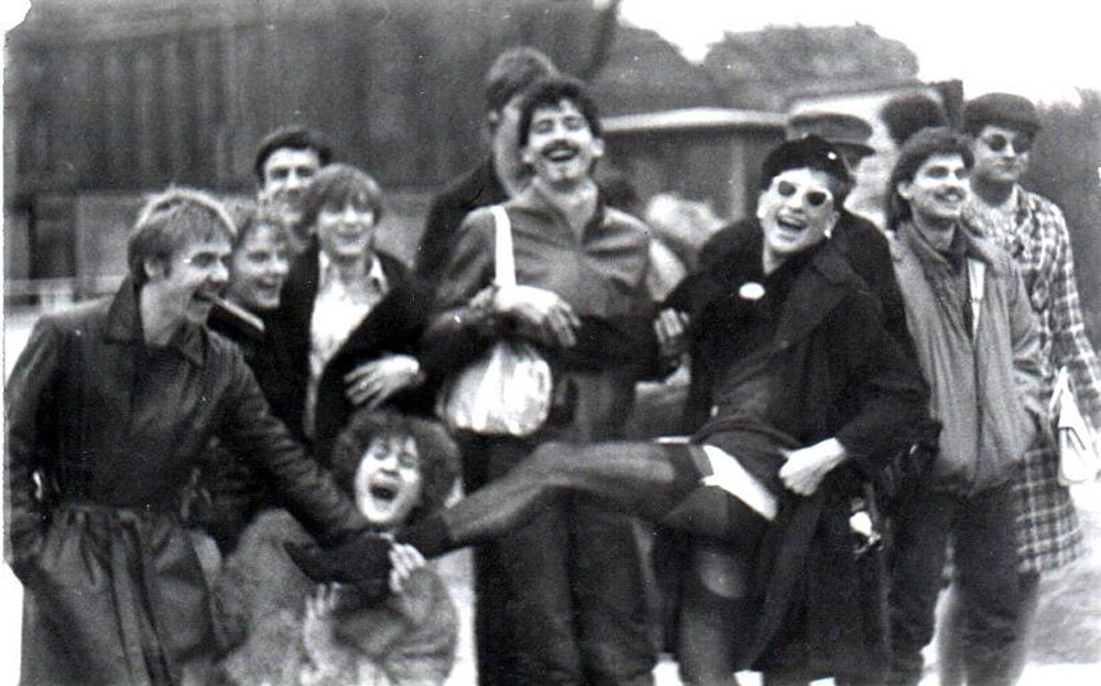 Eine Gruppe von 12 Personen, in der Mitte eine Person im Kleid mit Strapsen