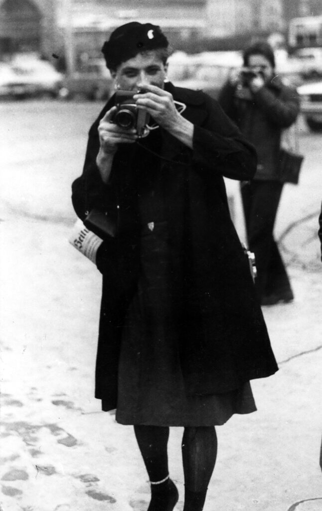 Eine Person im Fummel mit Fotoapparat in den Händen, im Hintergrund eine weitere Person mit Fotoapparat